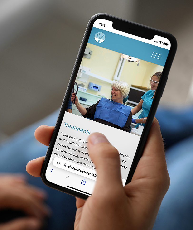 A hand is holding a mobile phone looking at the Island House Dental Care website